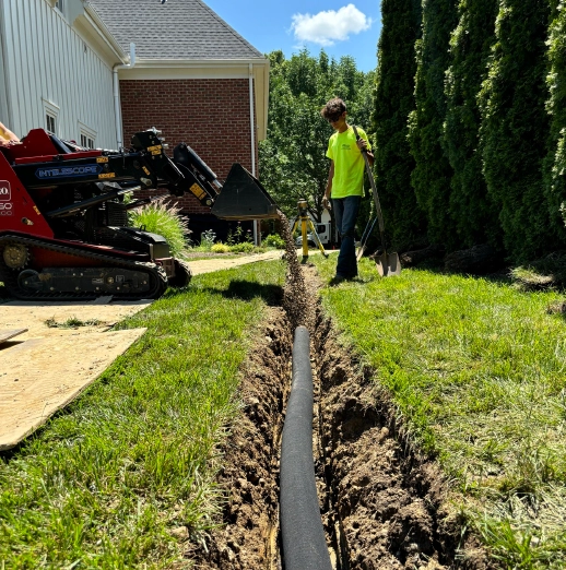 Drainage crew installing perforated pipe into a trench for a residential French drain system.